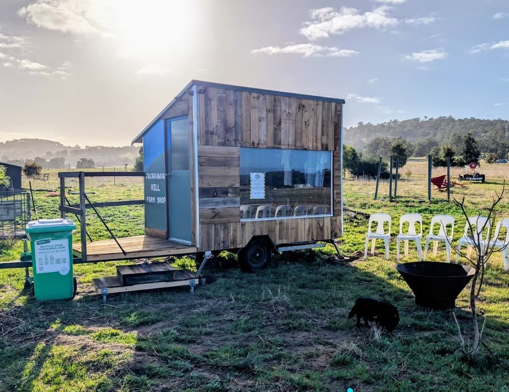 The timber Jacaranda Hill Farm Shop on a paddock at sunrise, with chairs and a fire pit beside it